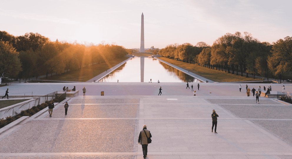 Washington Monument with reflecting pool and visitors at sunset.