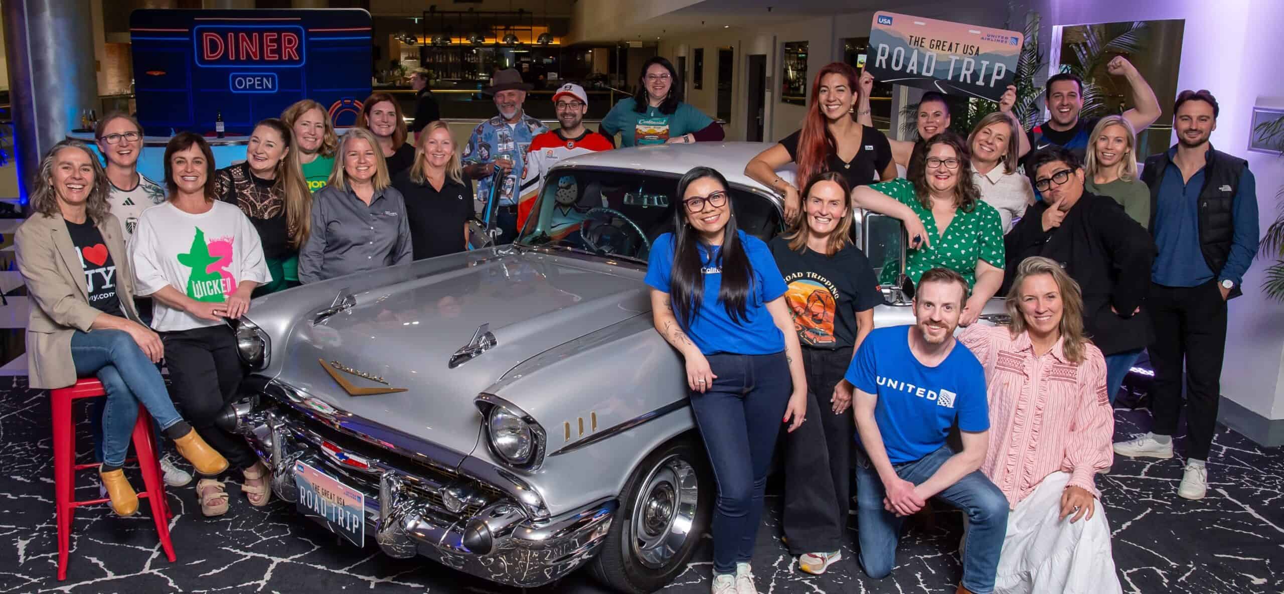 Group of people at The Brand USA road trip event with vintage car.