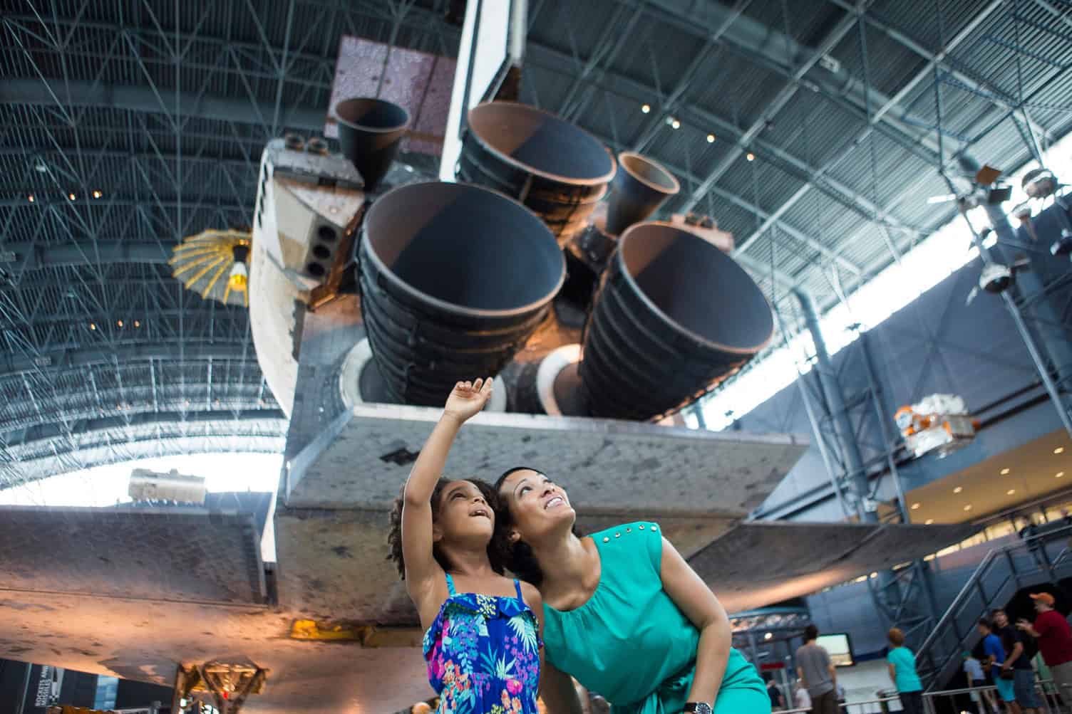 Two women looking up at a space shuttle exhibit in a museum.