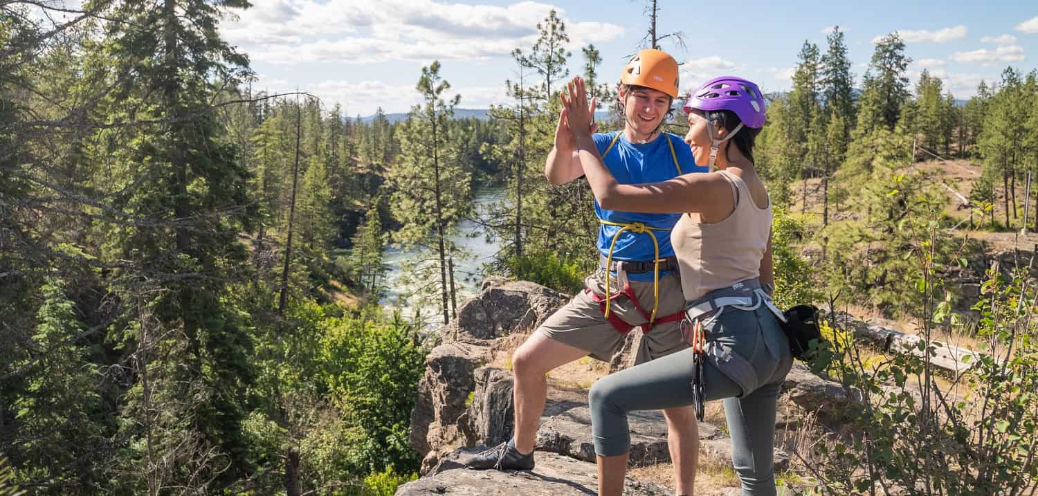 Two women climbers celebrating on a rocky ledge in a forested area.